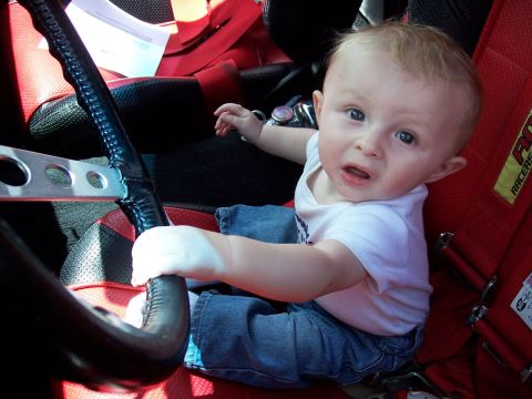 1972 Ford Ranchero - A baby sits in a red racing seat, gripping the steering wheel as if ready to drive.