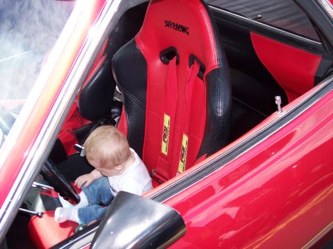 1972 Ford Ranchero - A baby sits in a red racing seat inside a vehicle.