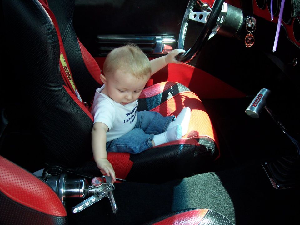 Baby sitting in a car's interior, reaching for keys near a Hurst shifter