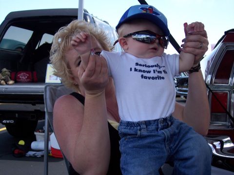 1972 Ford Ranchero - A baby dressed in sunglasses and a baseball cap is held by a woman, with vehicles visible in the background.