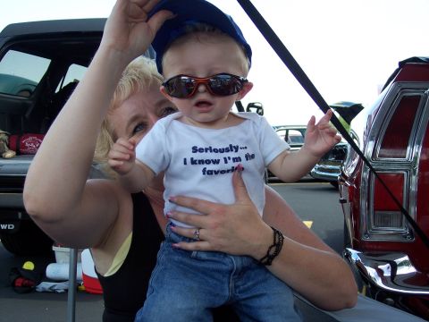 1972 Ford Ranchero - Baby with sunglasses and a blue cap is held by a woman, with vehicles in the background.