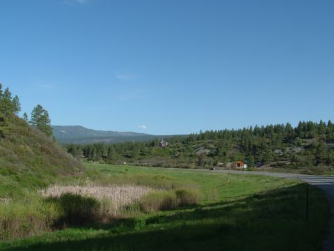 2007 Kawasaki Ninja - A scenic view of a rural landscape a road winding through green fields and dense forests under a bright blue sky.
