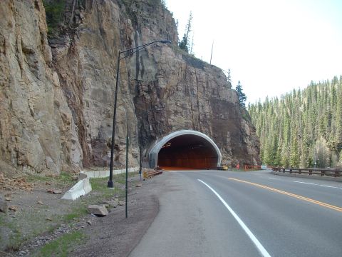 2007 Kawasaki Ninja - A road leads to a tunnel carved into a sheer rock face, surrounded by tall evergreen trees.