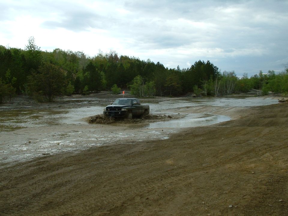 Dark pickup truck driving through mud, orange flag on antenna