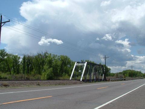 2007 Kawasaki Ninja - A metal truss railroad bridge spans over a two-lane road, with trees and power lines in the background under a dramatic sky.