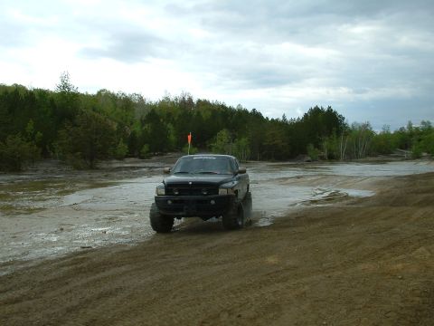 1991 Ford Bronco - A black pickup truck navigates a muddy terrain under a cloudy sky.