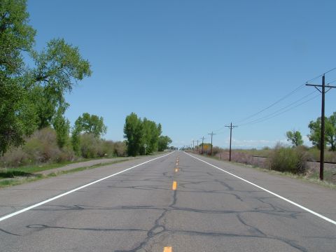 2007 Kawasaki Ninja - A long, straight highway disappears into the distance, bordered by green trees and a line of utility poles under a bright blue sky.