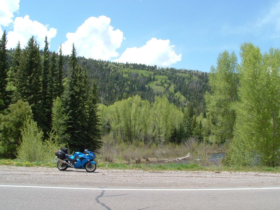 Blue 2007 Kawasaki Ninja motorcycle parked on a gravel shoulder next to a wooded hillside