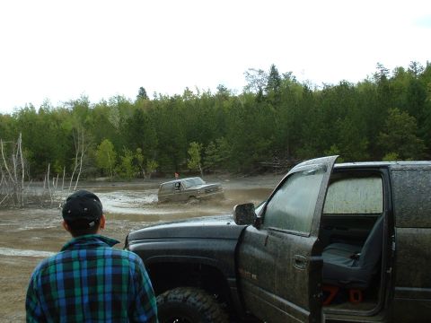 1991 Ford Bronco - Off-roading scene with two trucks navigating through a muddy terrain.