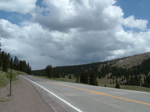 2007 Kawasaki Ninja - A scenic mountain road winds through a forested area with dramatic clouds overhead.