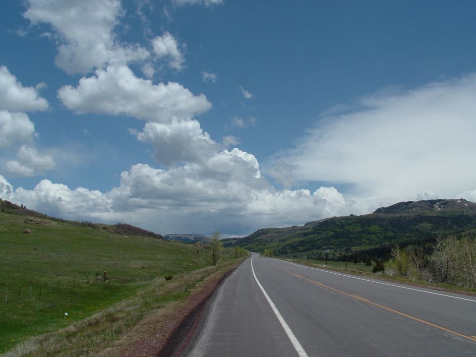 Highway stretching into distance with green hills and dramatic clouds