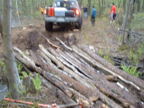 1991 Ford Bronco - A 1991 Ford Bronco navigates a challenging off-road course, using a makeshift bridge of logs to cross a muddy section of trail.