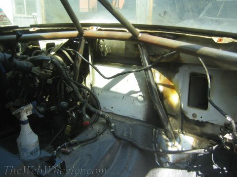 1990 Ford Bronco - Bare interior of a race-prepped vehicle showing a roll cage, exposed engine, wiring and a spray bottle.