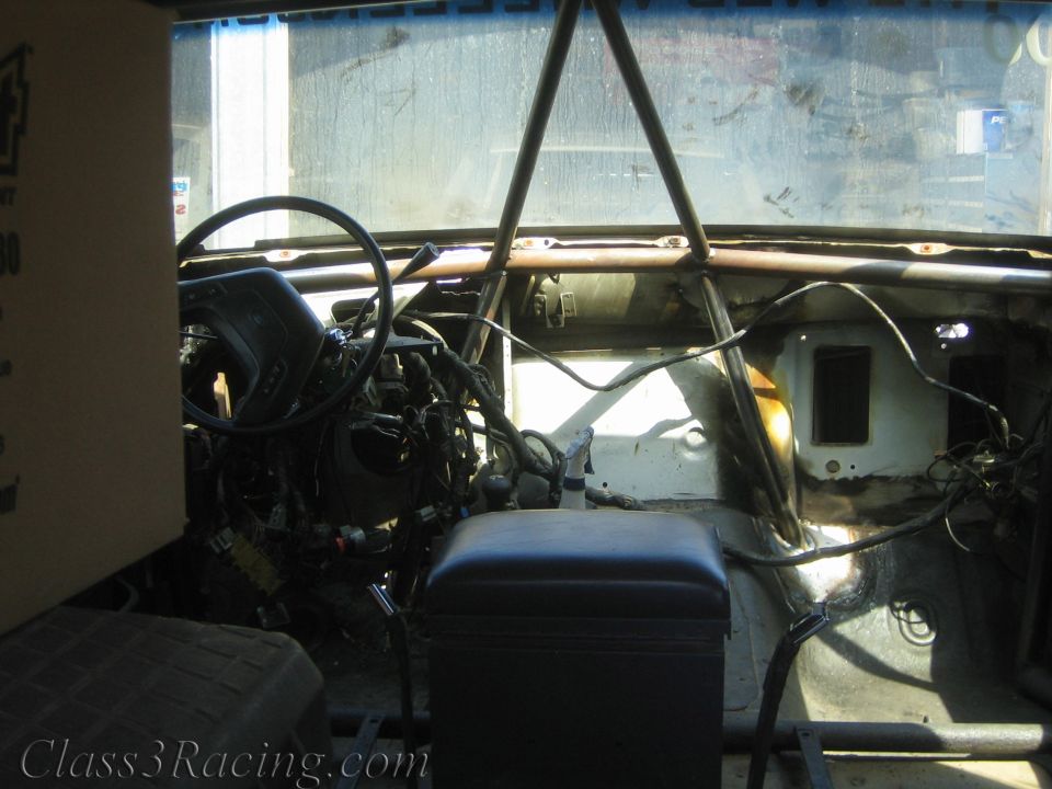 Stripped truck interior with roll cage, seat and exposed engine bay