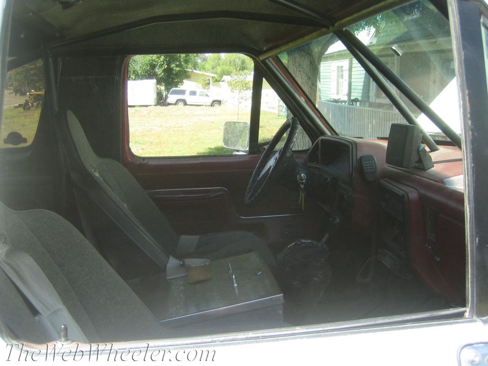 Interior of an old truck cab with red door panels, bench-style seat and floor shifter