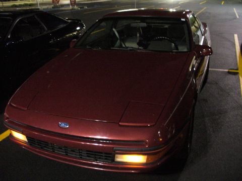 1991 Ford Probe - A maroon 1991 Ford Probe is parked next to another vehicle at night. The car is viewed from the front three-quarter angle.