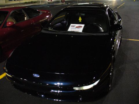 1991 Ford Probe - A dark blue coupe is parked in a lot at night, with a red car beside it and a sign on its dashboard.