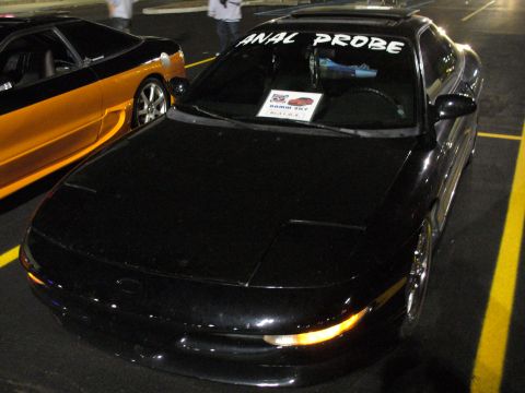 1991 Ford Probe - A black coupe is parked in a lot, with a humorous sticker on its windshield.