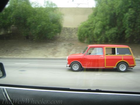 1990 Ford Bronco - red classic Mini estate wagon with wood-look side trim drives along a highway, photographed from a moving car.