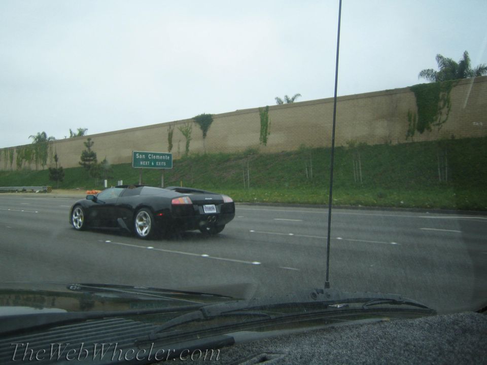 Black Lamborghini-style supercar on a freeway near a San Clemente sign