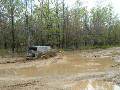 1991 Ford Bronco - A 1991 Ford Bronco navigates a muddy trail, kicking up water and mud as it gets stuck.