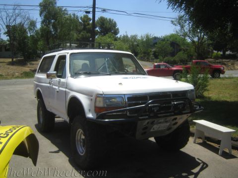 1990 Ford Bronco - white full-size SUV with a removable hardtop, roof rack and tubular front brush guard sits in a tree-lined yard.