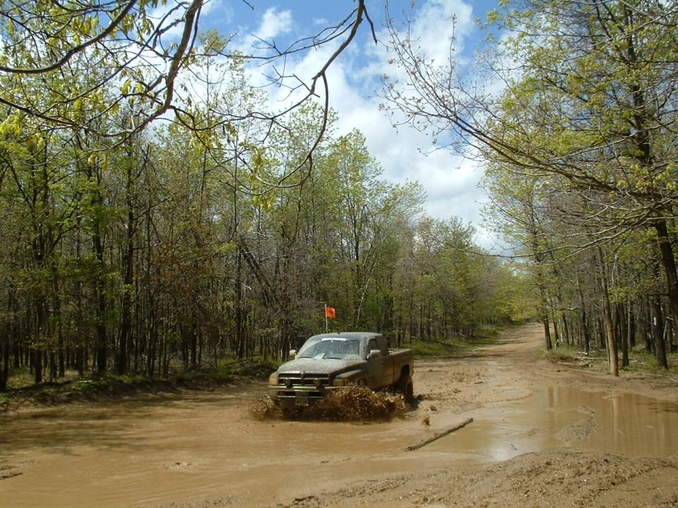 Mud-splattered truck driving through a muddy road with trees on both sides