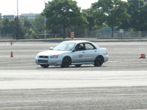 2001 Mercury Grand Marquis - A silver sedan with racing decals drives on a paved lot with orange cones.