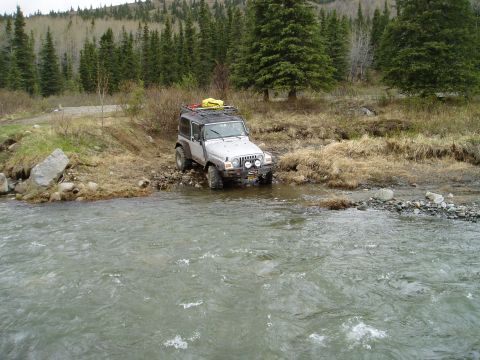 2000 Ford E350 - A Jeep Wrangler navigates a rocky stream bed in a wooded, mountainous area.