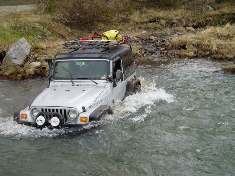 2000 Ford E350 - A silver Jeep Wrangler Rubicon navigates a river, its tires kicking up water.