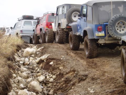 2000 Ford E350 - Several modified off-road vehicles are lined up on a muddy, rocky trail.