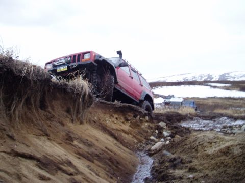 2000 Ford E350 - A red Jeep Cherokee XJ navigates a challenging muddy terrain with a snorkel attachment.