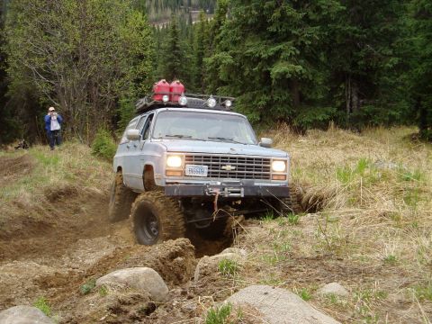 2000 Ford E350 - This lifted SUV is shown tackling a challenging off-road course with a person observing in the background.