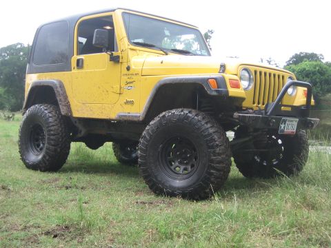 2001 Jeep Wrangler - Yellow 2001 Jeep Wrangler with off-road tires sits on grassy terrain.