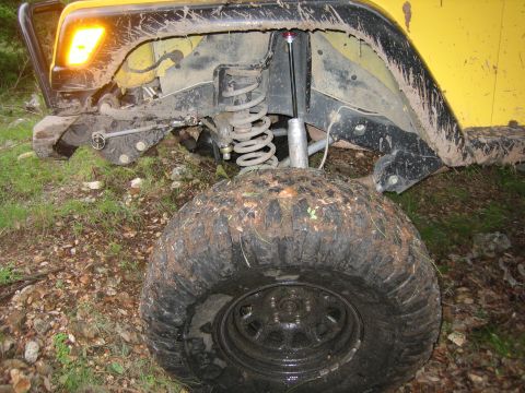 2001 Jeep Wrangler - Front suspension and tire of a muddy 2001 Jeep Wrangler off-road.