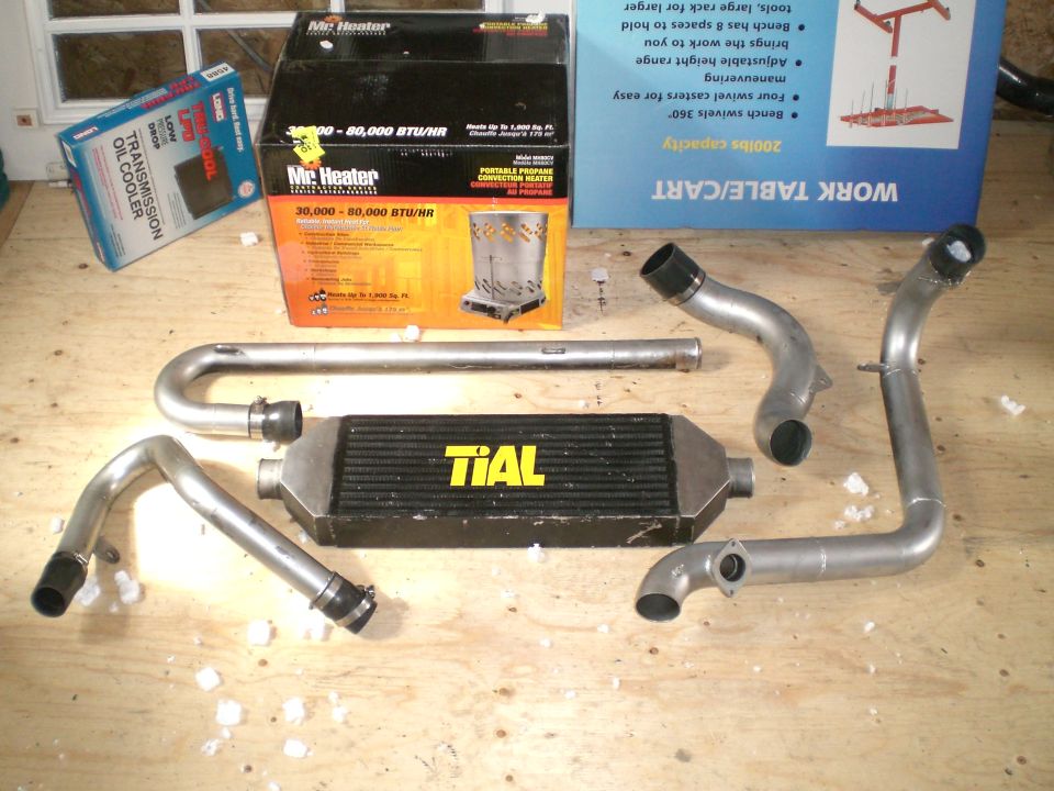 TiAL front-mount intercooler and four aluminum charge pipes laid out on plywood bench