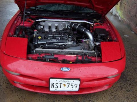 1995 Ford Probe - The engine bay of a red 1995 Ford Probe is visible with the hood open, revealing the motor and front grille.