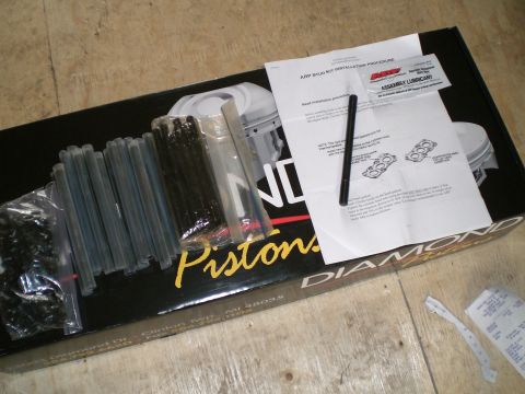 1995 Ford Probe - An ARP head stud kit laid out on a black Diamond Pistons box on a plywood floor: rows of black-oxide studs in plastic sleeves, a bag of nut…