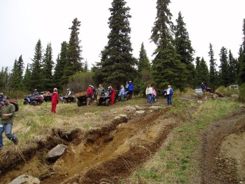 2000 Ford E350 - A group of people and ATVs are gathered in a wooded area, with muddy tracks indicating off-road activity.
