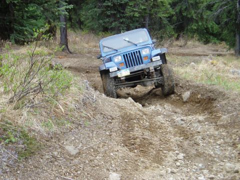 2000 Ford E350 - A blue Jeep Wrangler navigates a challenging off-road trail with steep inclines and rough terrain.