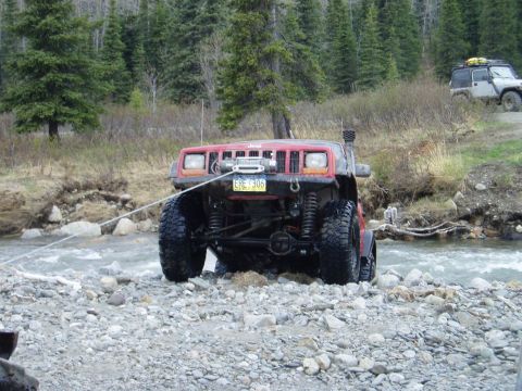 2000 Ford E350 - A red Jeep Cherokee is being pulled through a rocky stream, with another Jeep parked on the higher ground nearby.