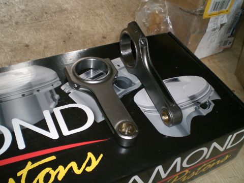 1995 Ford Probe - Close-up of two forged H-beam connecting rods with bronze wrist-pin bushings and capscrew big ends, sitting on a black Diamond Pistons cart…