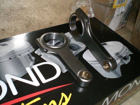1995 Ford Probe - Two forged H-beam connecting rods with bronze small-end bushings and shot-peened surfaces resting on a Diamond Pistons box printed with pis…