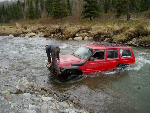 2000 Ford E350 - A red Jeep Cherokee navigates a river crossing, with a person on the hood checking the water depth.