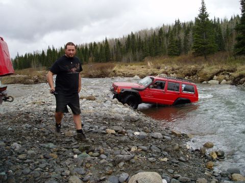 2000 Ford E350 - A red Jeep Cherokee navigates a rocky stream bed with a man observing from the bank.