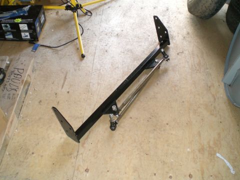 1995 Ford Probe - A freshly painted black steel bracket assembly with drilled mounting flanges at each end and a bolt-on adjustable link rod, laid on a plywo…