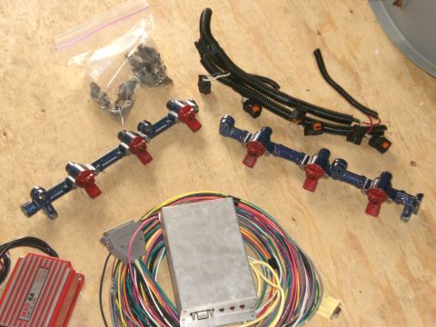 1995 Ford Probe - Standalone engine-management parts spread on a plywood bench: a pair of blue metal-flake fuel rails with red fuel injectors, a loom-wrapped…