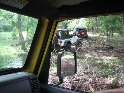 2001 Jeep Wrangler - Two Jeep Wranglers navigate a wooded trail, one white and one red, with a stream nearby.