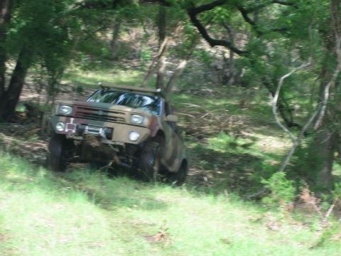 2001 Jeep Wrangler - A camouflaged off-road vehicle navigates a wooded area with a winch mounted on its front.