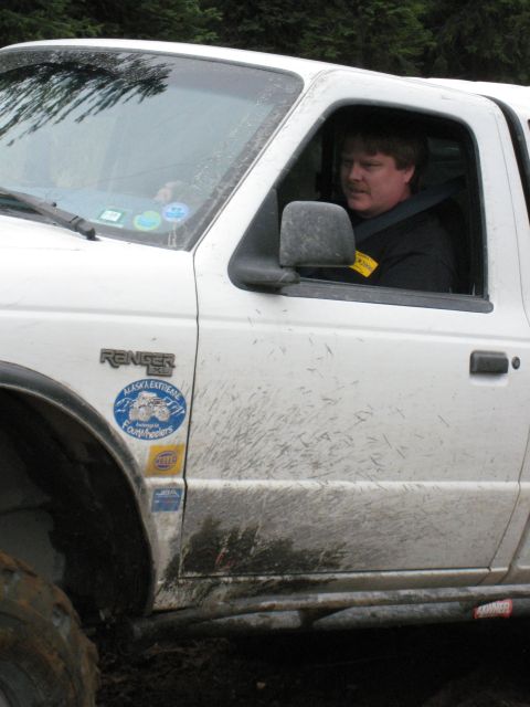 2000 Ford E350 - A muddy white Ford Ranger pickup truck with off-road stickers is driven by a man.